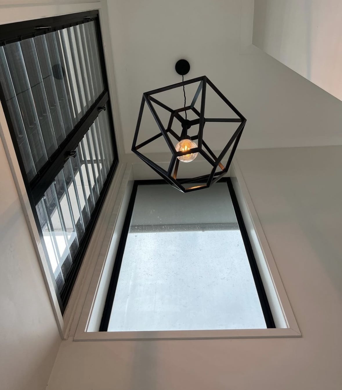 A modern feauture light in a stairway with a big window next to it.