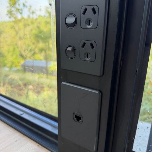 Black power socket mounted on a black wall next to a window.