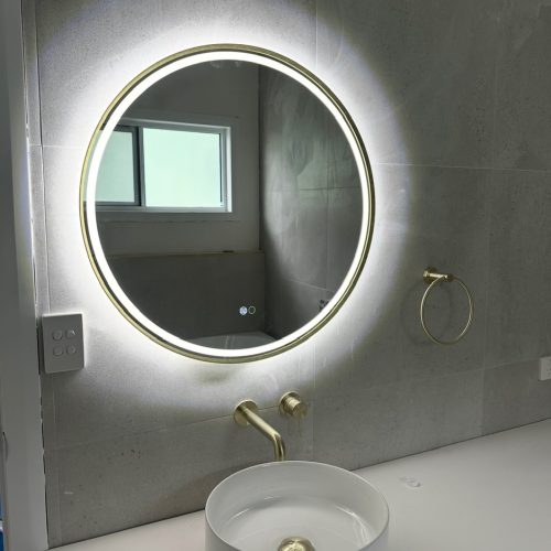 A circular bathroom mirror with backlighting above a modern sink.